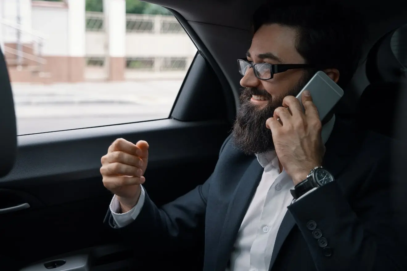 Spokojný podnikateľ v obleku telefonuje počas pohodlnej jazdy v luxusnom taxíku spoločnosti Grouptrans. Komfortná preprava pre biznis klientelu.